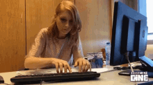 a woman sits at a desk typing on a keyboard with a screen behind her that says tellement cine