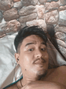 a man with a beard is laying on a bed with a stone wall behind him