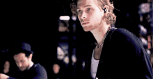 a man with curly hair is wearing a necklace and earbuds while holding a guitar .
