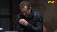 a man is sitting at a table with his hand on his chin and a sas advertisement behind him