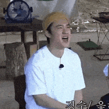 a man wearing a yellow hat and a white shirt is sitting in front of a fan .