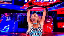 a woman in a checkered shirt is holding a wrestling championship belt over her head .