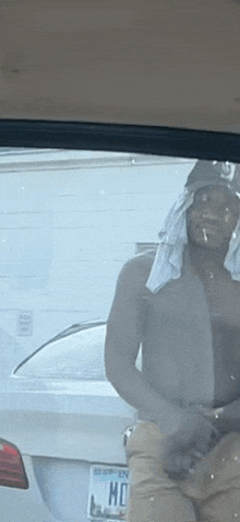 a man without a shirt is standing in front of a car with a towel around his head .