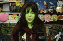 a woman with green paint on her face is standing in front of a shelf with stuffed animals