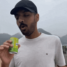 a man wearing a black calvin klein hat is drinking a can of soda