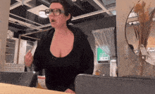 a woman wearing glasses and a black top stands in a room