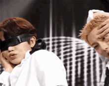 two men wearing blindfolds are standing next to each other and one has his hand on his forehead .