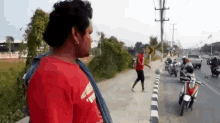 a man wearing a red shirt that says ' easy rider ' on it stands on a sidewalk