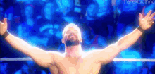 a wrestler is standing in a ring with his arms outstretched in front of a crowd .