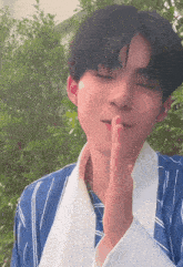 a young man wearing a blue and white striped shirt holds his finger to his lips