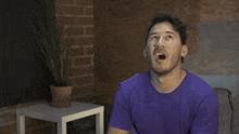 a man in a purple shirt stands in front of a microphone with his mouth open