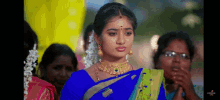 a woman in a blue saree is standing in a crowd of people .