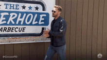 a man is standing in front of a sign that says the erhole barbeque .