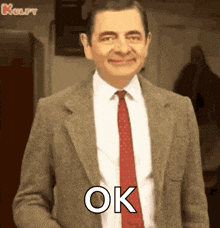 mr bean is wearing a suit and tie and is smiling and says ok .