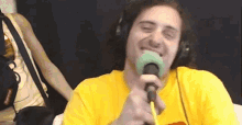 a man in a yellow shirt is singing into a microphone .