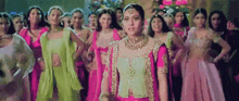 a woman in a pink dress is standing in front of a crowd of women in traditional indian clothing .