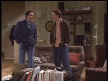 two men are standing in a living room with a dart board in the background .