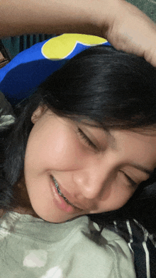 a girl with braces on her teeth is laying on a bed with a pillow on her head