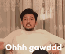 a man with a beard is sitting on a couch with the words ohhh gawdd on the screen
