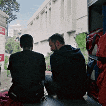 two men sit on the back of a truck in front of a building with a sign that says no smoking