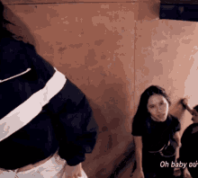a woman in a black shirt is standing in front of a wall with the words oh baby on it