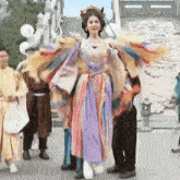 a woman in a colorful dress with wings is standing in front of a group of people