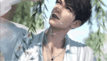 a man wearing a necklace and a blue shirt is looking up at the sky .