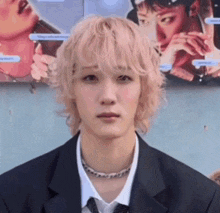 a young man with blonde hair and a suit and tie is standing in front of a wall .
