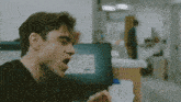 a man in a black shirt is yawning in front of a computer monitor