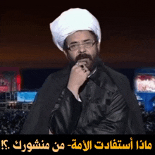 a man wearing glasses and a white turban stands in front of a sign that says ' arabic '