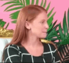 a woman with red hair is standing in front of a pink wall with palm trees .