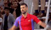 a man in a red and purple shirt is standing in front of a crowd of people .