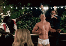 a shirtless man in white underwear is pouring champagne into his mouth