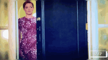 a woman in a purple dress is standing in a doorway with smp in the corner