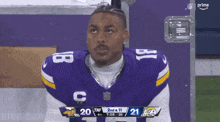 a football player with the number 18 on his jersey looks up at the scoreboard