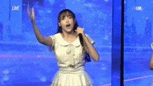 a woman in a white dress is dancing in front of a blue screen .