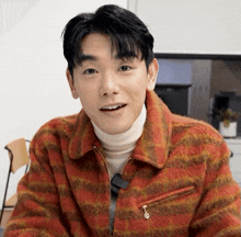a man wearing a plaid jacket and a white turtleneck smiles for the camera