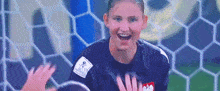 a female soccer goalie is smiling while standing in front of a soccer net .