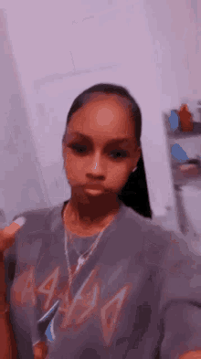 a woman wearing a t-shirt and a necklace is taking a selfie in a room .