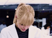 a woman wearing a lab coat and a ponytail is looking down