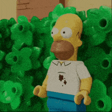 a lego homer simpson is standing in front of a wall of green flowers