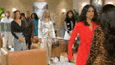 a group of women are standing in a living room . one of the women is wearing a red dress .