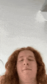 a young man with long red hair is making a funny face .