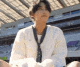 a young man wearing a tie and a white sweater is sitting in front of a stadium .