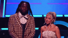 a man in a plaid jacket stands next to a woman in a strapless dress on a stage