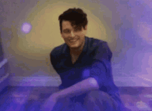 a man in a green shirt is sitting on the floor with purple lights behind him .