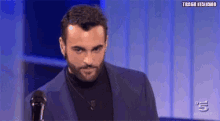 a man with a beard is wearing a blue suit and black turtleneck sweater .