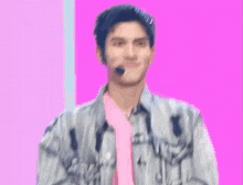 a young man wearing a pink shirt and a denim jacket with a microphone on his head .