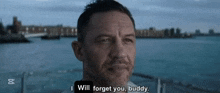 a man with a beard is standing in front of a body of water and says i will forget you buddy .