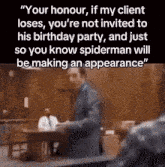 a man in a suit is standing in front of a table in a courtroom and talking to someone .